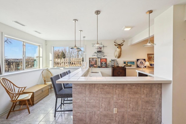 kitchen with sink, a breakfast bar area, decorative light fixtures, light tile patterned floors, and kitchen peninsula