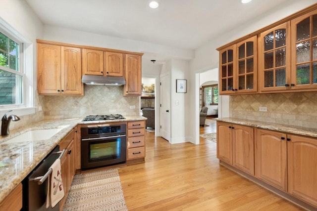 kitchen with sink, appliances with stainless steel finishes, light stone counters, light hardwood / wood-style floors, and decorative backsplash