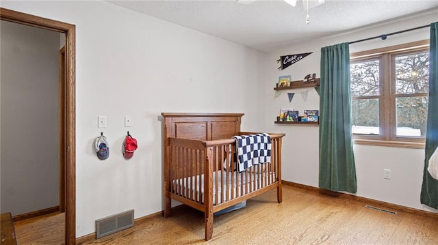 bedroom featuring hardwood / wood-style floors, a crib, and a textured ceiling