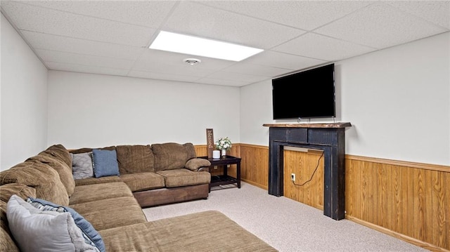 carpeted living room featuring a drop ceiling and wooden walls