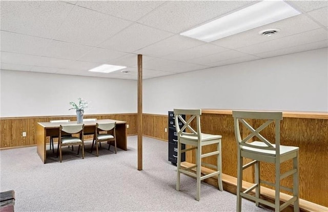 dining room with carpet, bar, a drop ceiling, and wooden walls