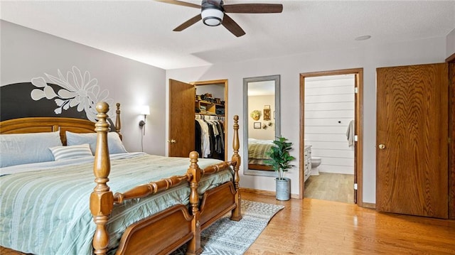 bedroom with ensuite bathroom, a walk in closet, wood-type flooring, a closet, and ceiling fan