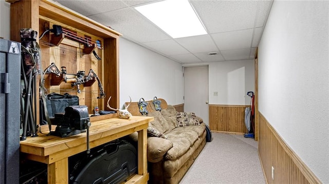 interior space featuring light carpet, wooden walls, and a paneled ceiling