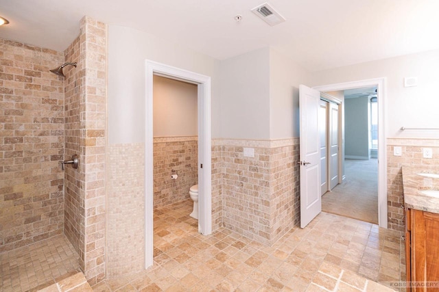 bathroom featuring tile walls, vanity, toilet, and tiled shower