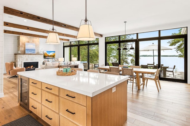 kitchen with pendant lighting, beverage cooler, light hardwood / wood-style floors, light brown cabinets, and beam ceiling