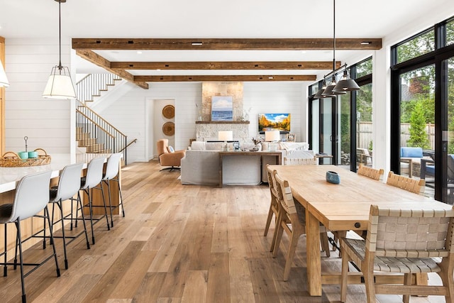 dining space with wood walls, beam ceiling, and light wood-type flooring