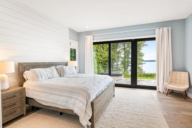 bedroom featuring light hardwood / wood-style flooring, access to outside, wooden walls, and a water view