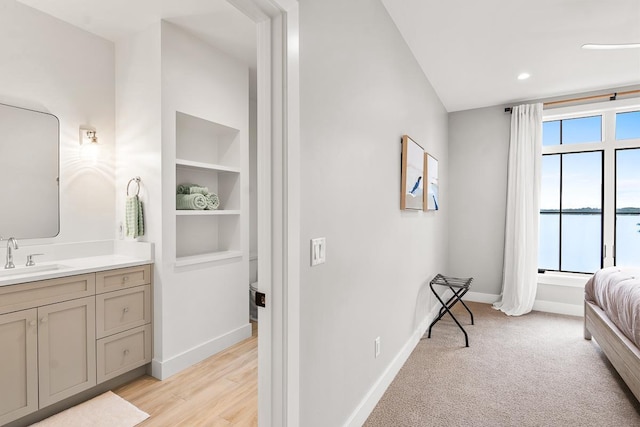 bedroom with sink, light colored carpet, and a water view