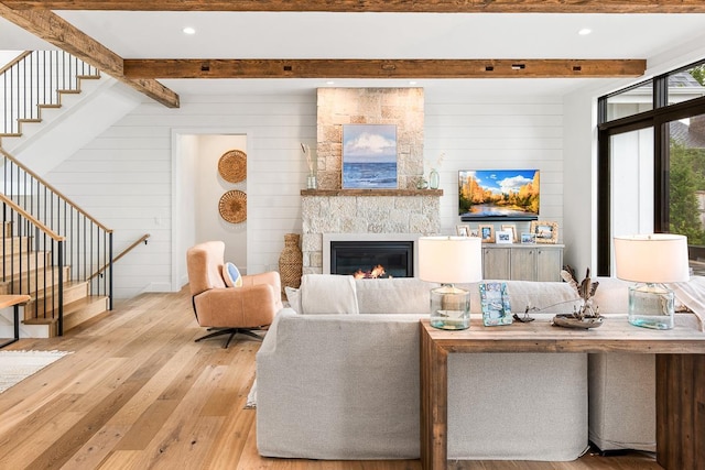 living room with beamed ceiling, wooden walls, a fireplace, and light hardwood / wood-style flooring