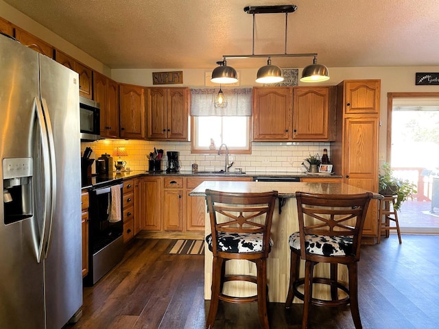 kitchen with sink, a breakfast bar area, hanging light fixtures, stainless steel appliances, and dark wood-type flooring