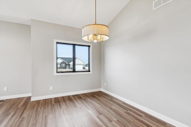 empty room with wood-type flooring, vaulted ceiling, and a notable chandelier