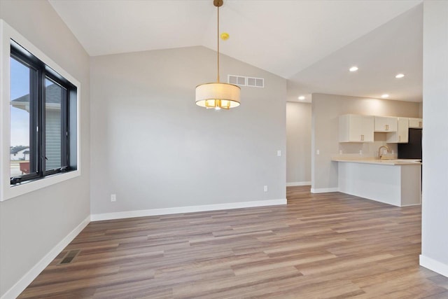 unfurnished room featuring lofted ceiling, sink, and light hardwood / wood-style floors