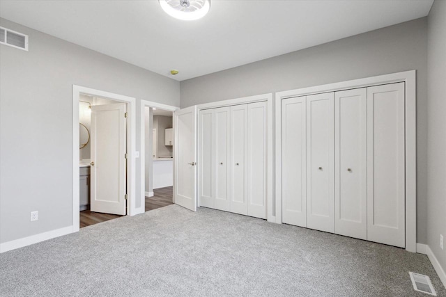 unfurnished bedroom featuring dark carpet, two closets, and ensuite bath