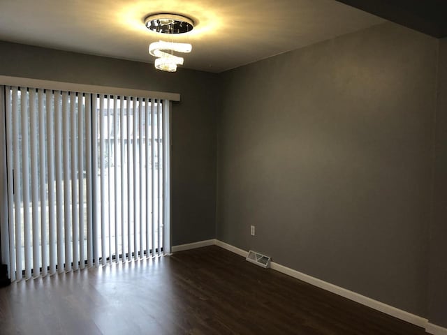 spare room with dark wood-type flooring and a chandelier