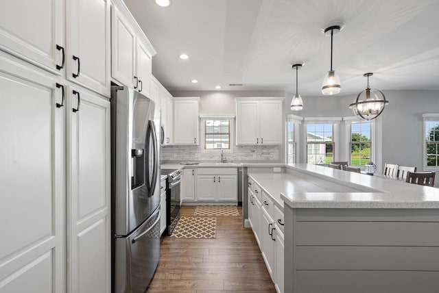 kitchen with pendant lighting, appliances with stainless steel finishes, backsplash, white cabinets, and a kitchen island