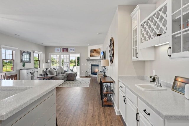 kitchen with white cabinetry, a stone fireplace, sink, and dark wood-type flooring