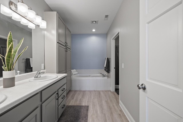 bathroom featuring hardwood / wood-style floors, vanity, and tiled bath