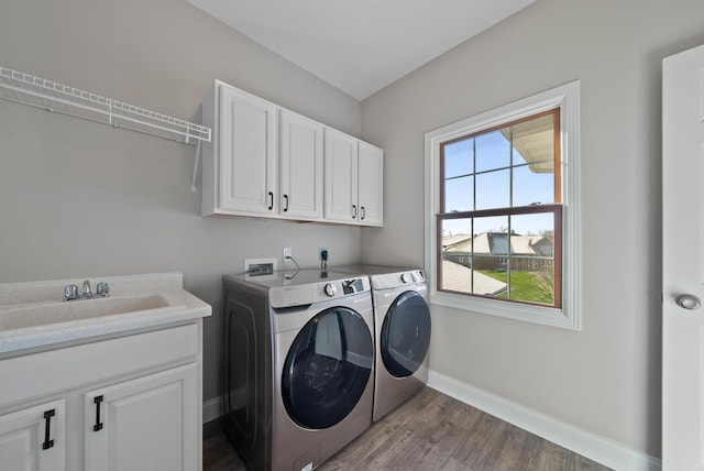 laundry room featuring sink, hardwood / wood-style floors, washing machine and dryer, and cabinets