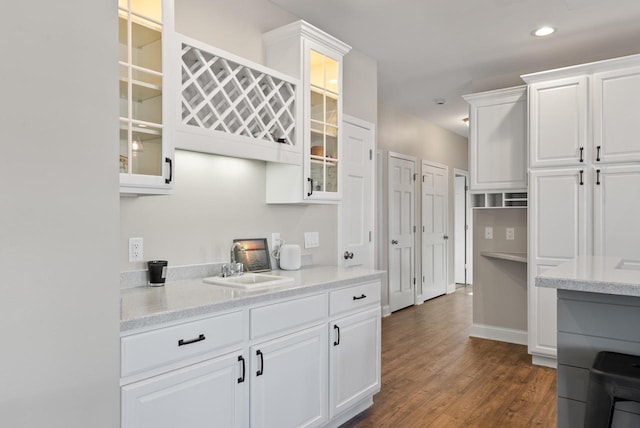 kitchen with dark hardwood / wood-style flooring, sink, light stone counters, and white cabinets