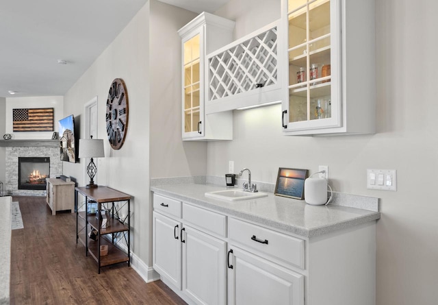 bar with sink, dark wood-type flooring, white cabinets, and a fireplace