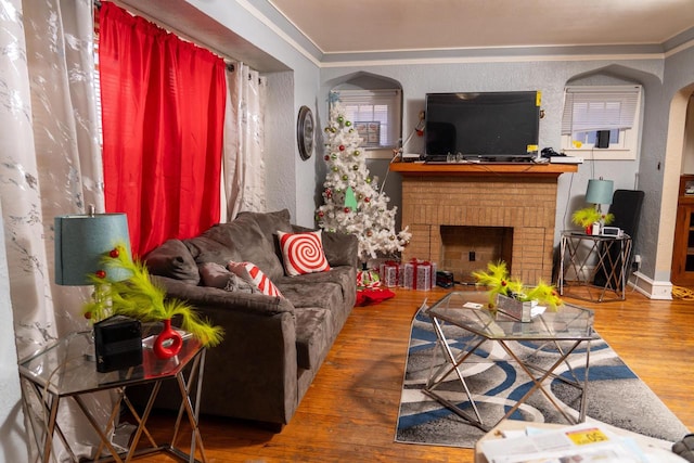 living room with ornamental molding, wood-type flooring, and a brick fireplace