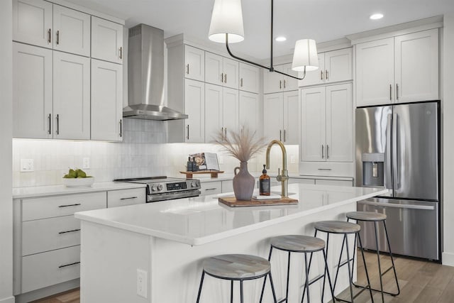 kitchen with stainless steel appliances, pendant lighting, a center island with sink, and wall chimney exhaust hood