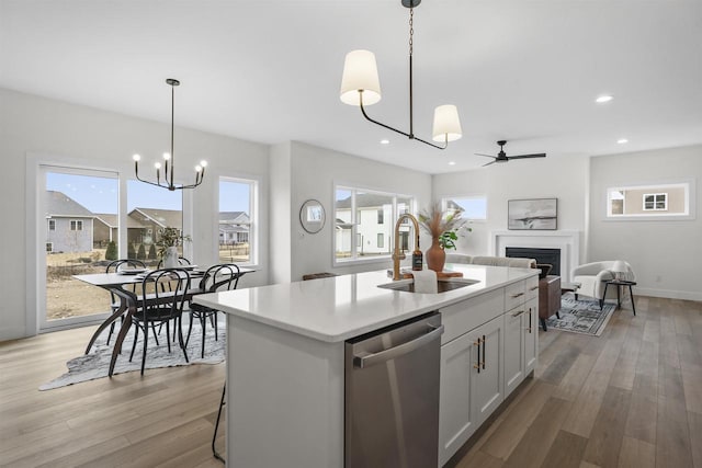 kitchen featuring sink, dishwasher, a kitchen island with sink, white cabinets, and decorative light fixtures