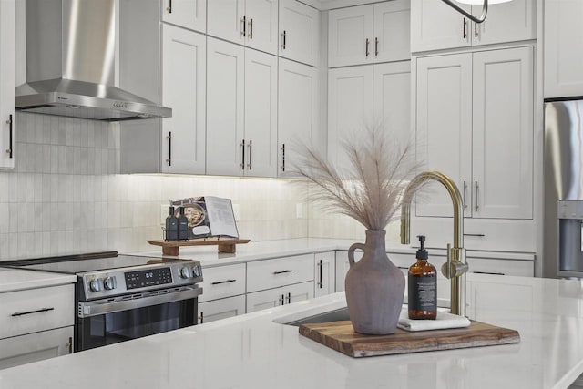 kitchen featuring white cabinetry, decorative backsplash, stainless steel appliances, and wall chimney exhaust hood