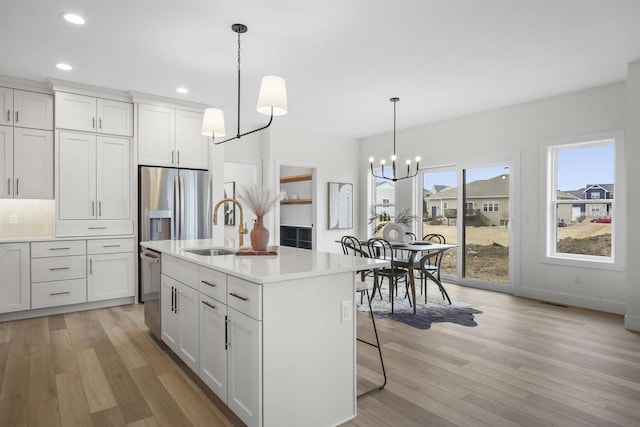 kitchen with sink, an inviting chandelier, white cabinetry, hanging light fixtures, and a kitchen island with sink