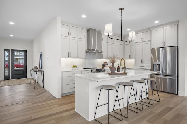 kitchen with white cabinetry, decorative light fixtures, appliances with stainless steel finishes, an island with sink, and wall chimney range hood