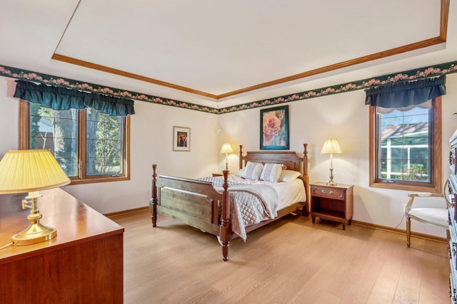 bedroom with multiple windows, a tray ceiling, ornamental molding, and light hardwood / wood-style floors