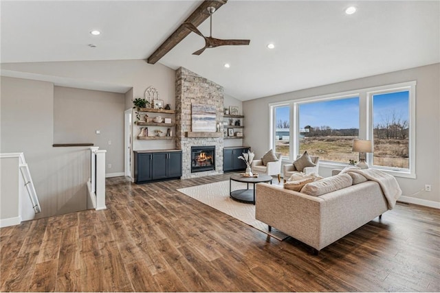 living room with ceiling fan, a stone fireplace, vaulted ceiling with beams, and dark hardwood / wood-style floors