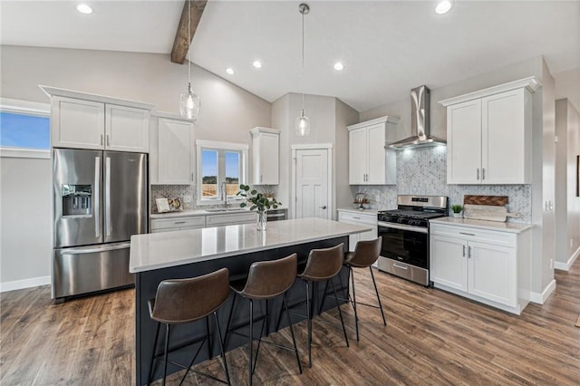 kitchen featuring sink, white cabinetry, hanging light fixtures, appliances with stainless steel finishes, and wall chimney range hood