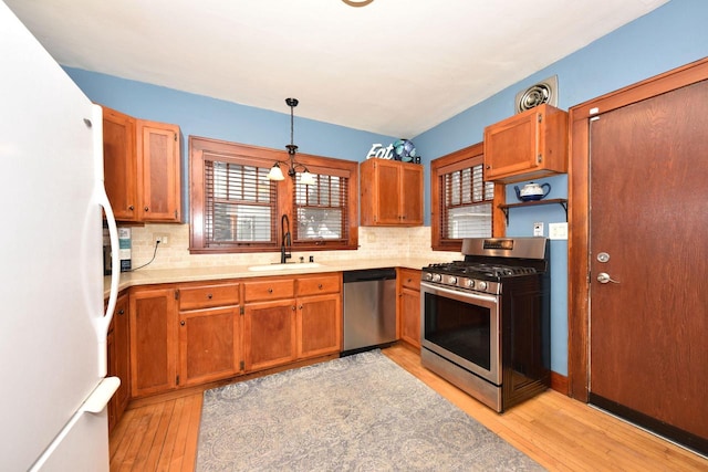 kitchen featuring pendant lighting, sink, light hardwood / wood-style flooring, appliances with stainless steel finishes, and tasteful backsplash