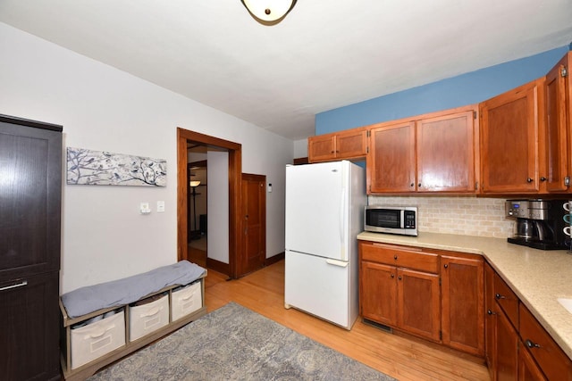 kitchen with white refrigerator, backsplash, and light wood-type flooring