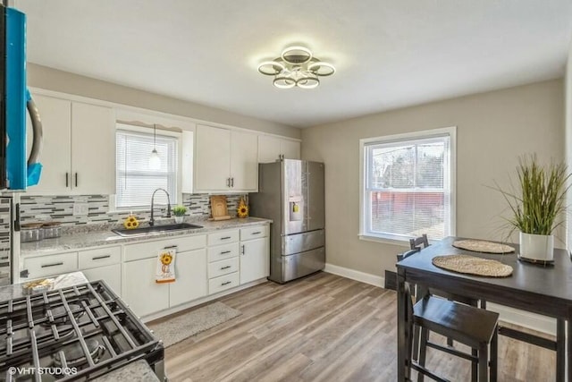 kitchen with sink, stainless steel refrigerator with ice dispenser, light stone countertops, white cabinets, and decorative backsplash