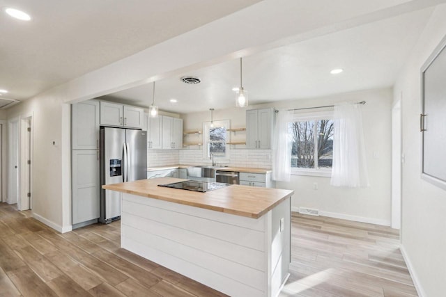 kitchen with hanging light fixtures, stainless steel appliances, a kitchen island, wood counters, and decorative backsplash