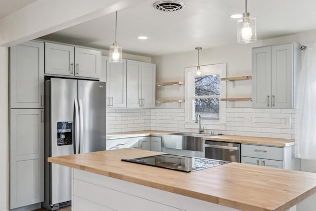 kitchen featuring stainless steel appliances, a kitchen island, pendant lighting, and wood counters