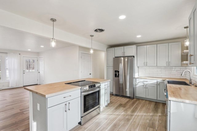 kitchen featuring sink, butcher block countertops, a center island, hanging light fixtures, and appliances with stainless steel finishes