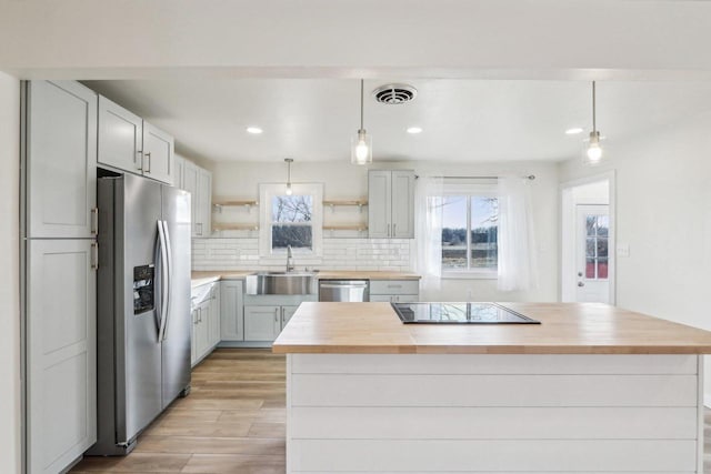 kitchen featuring appliances with stainless steel finishes, decorative light fixtures, a center island, and sink