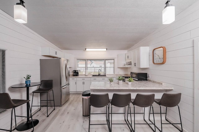 kitchen featuring kitchen peninsula, a kitchen breakfast bar, stainless steel refrigerator, and white cabinets