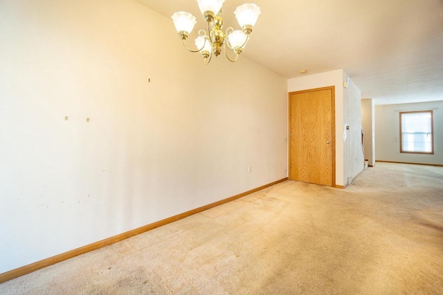 spare room featuring light carpet, a notable chandelier, and baseboards