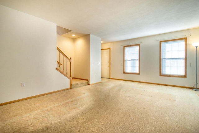 unfurnished room featuring stairs, light carpet, and baseboards