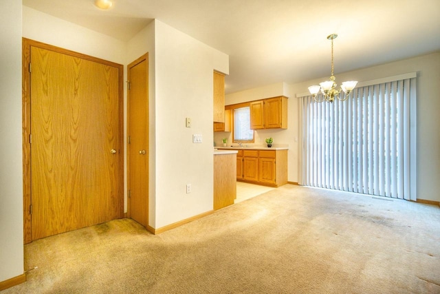 kitchen with baseboards, light colored carpet, a notable chandelier, light countertops, and a sink