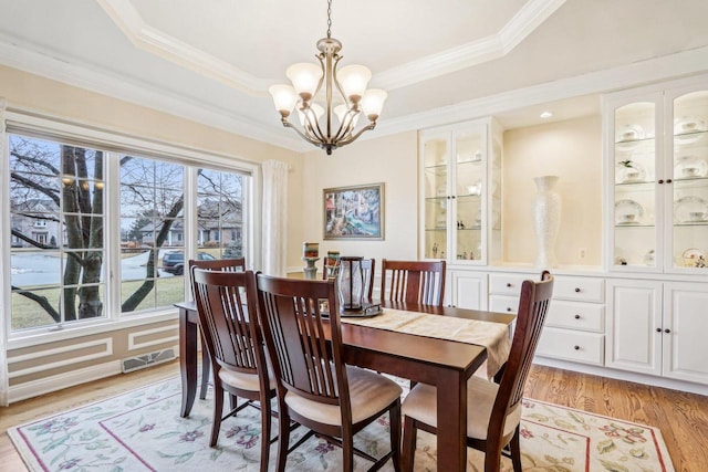 dining room with an inviting chandelier, ornamental molding, a raised ceiling, and light hardwood / wood-style floors