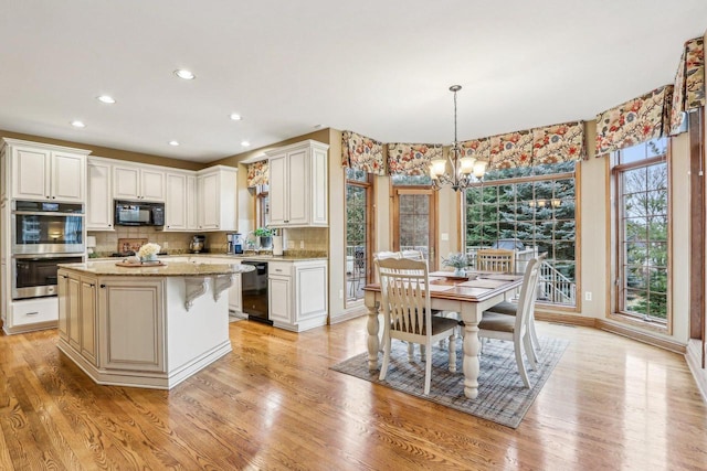 kitchen with white cabinets, hanging light fixtures, a center island, light stone counters, and black appliances