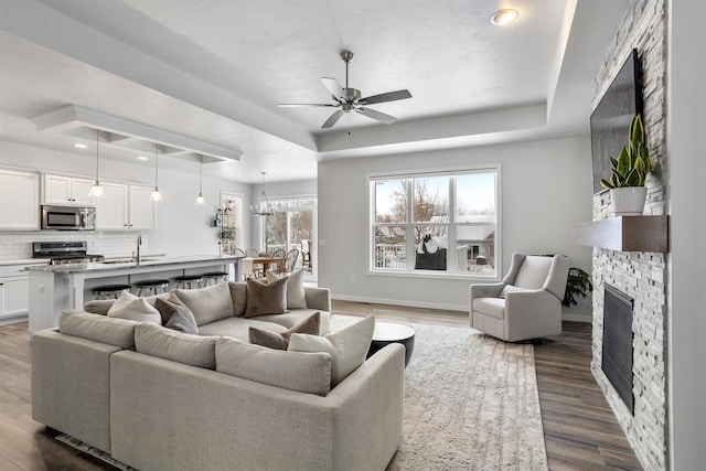 living room with sink, ceiling fan, a tray ceiling, a fireplace, and dark hardwood / wood-style flooring