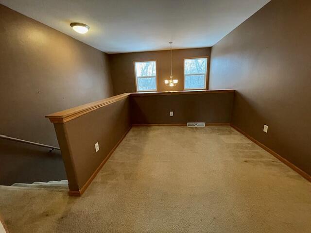 spare room featuring light colored carpet and an inviting chandelier