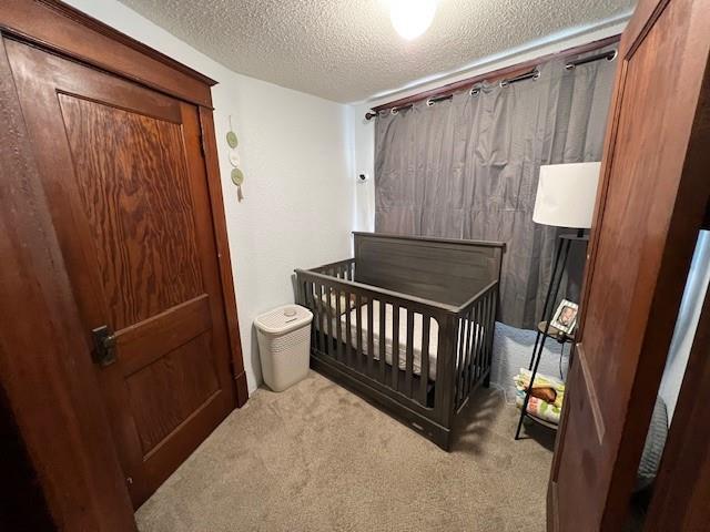 bedroom with light colored carpet, a nursery area, and a textured ceiling