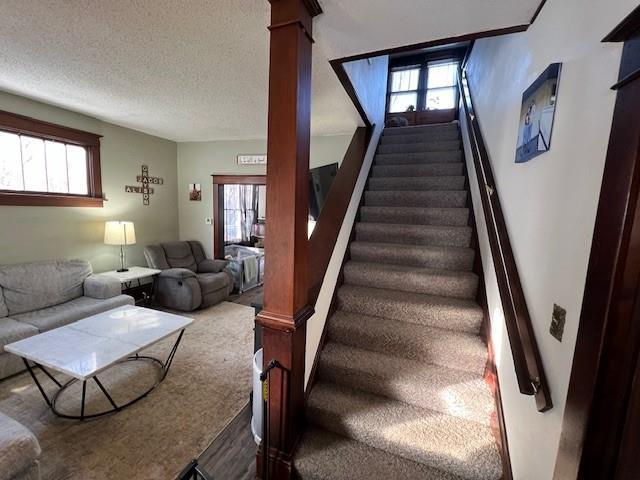 stairs with a wealth of natural light, a textured ceiling, and ornate columns